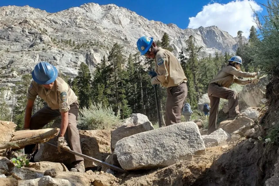 An Inyo Backcountry Trail Crew uses rock bars and other hand tools to build new trail out of rock.
